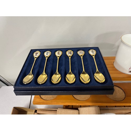 121 - 12 boxed Hummel mugs along with 12 boxed Hummel teaspoons & wooden wall display rack.