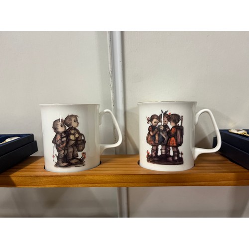 121 - 12 boxed Hummel mugs along with 12 boxed Hummel teaspoons & wooden wall display rack.