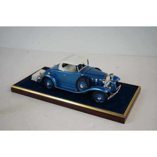 1169 - Five cased 1:18 scale diecast model classic cars to include BMW, Jaguar etc, models fixed to a woode... 