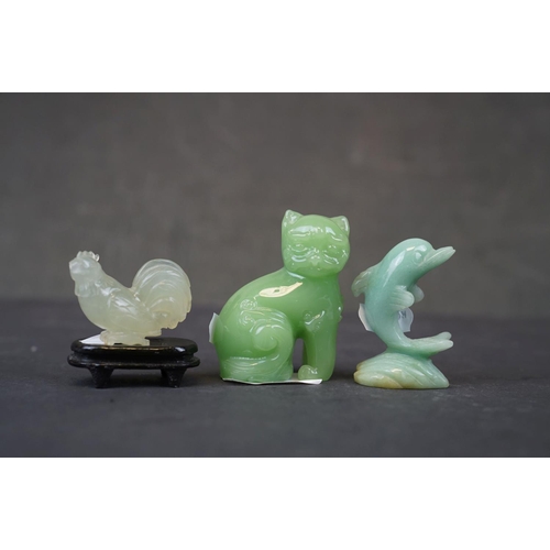 282 - A collection of three oriental carved jade animals to include a cat, dolphin and a cockerel on woode... 