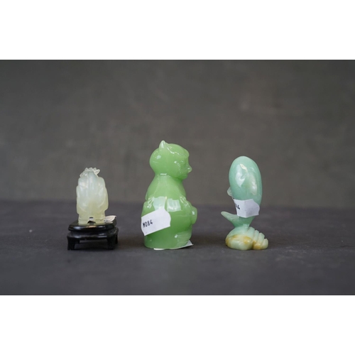 282 - A collection of three oriental carved jade animals to include a cat, dolphin and a cockerel on woode... 