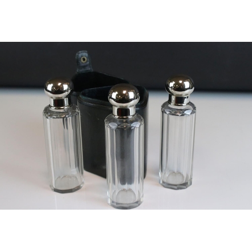 95 - Three glass perfume / cologne bottles with silver plated screw top lids and glass stoppers in a fitt... 