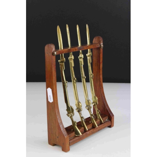 63 - Four Trench Art Brass Desk Paperknives in the form of  Rifles contained within a wooden gun rack, 20... 