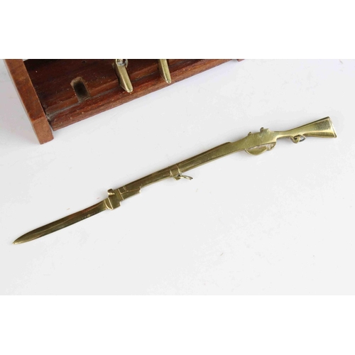 63 - Four Trench Art Brass Desk Paperknives in the form of  Rifles contained within a wooden gun rack, 20... 