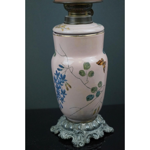 641 - A pink ground ceramic oil lamp decorated with butterflies and fauna, mounted on a metal base, of roc... 