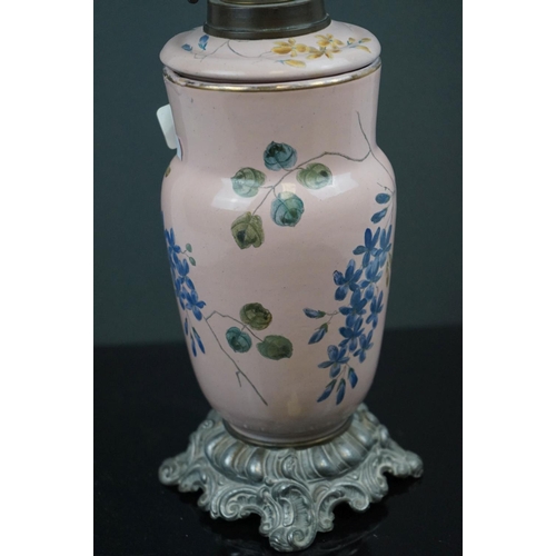 641 - A pink ground ceramic oil lamp decorated with butterflies and fauna, mounted on a metal base, of roc... 