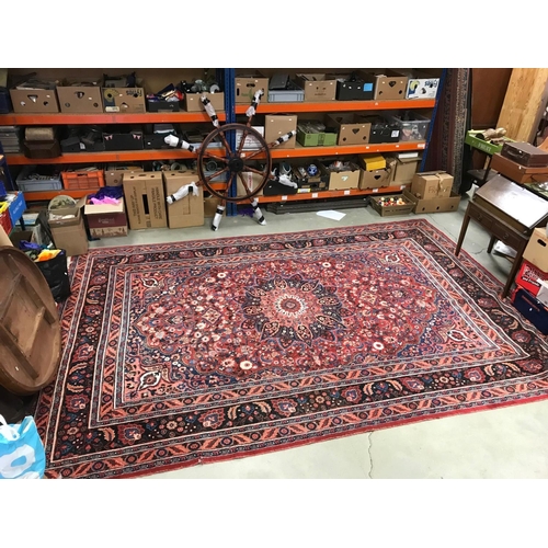 821 - Large Eastern Wool Hand Knotted Rug, red ground with a floral patterned central panel surrounded by ... 