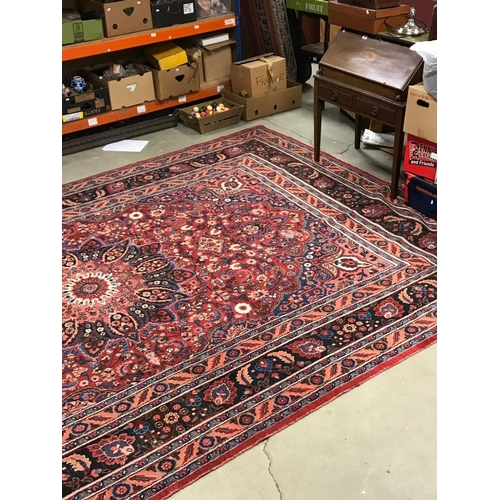 821 - Large Eastern Wool Hand Knotted Rug, red ground with a floral patterned central panel surrounded by ... 