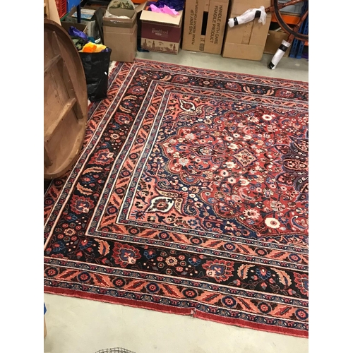 821 - Large Eastern Wool Hand Knotted Rug, red ground with a floral patterned central panel surrounded by ... 