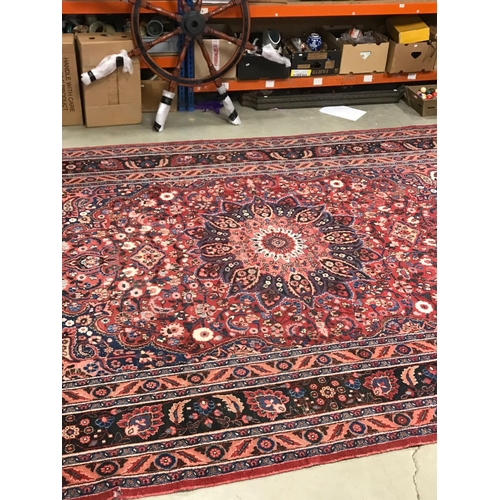 821 - Large Eastern Wool Hand Knotted Rug, red ground with a floral patterned central panel surrounded by ... 