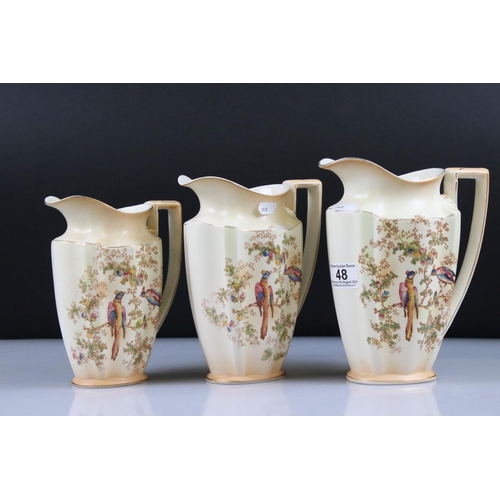 48 - Set of Three Crown Ducal Graduating Blush Ivory Jugs decorated with exotic birds, largest 22cm