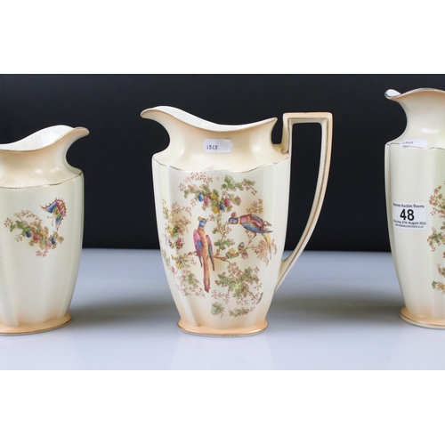 48 - Set of Three Crown Ducal Graduating Blush Ivory Jugs decorated with exotic birds, largest 22cm