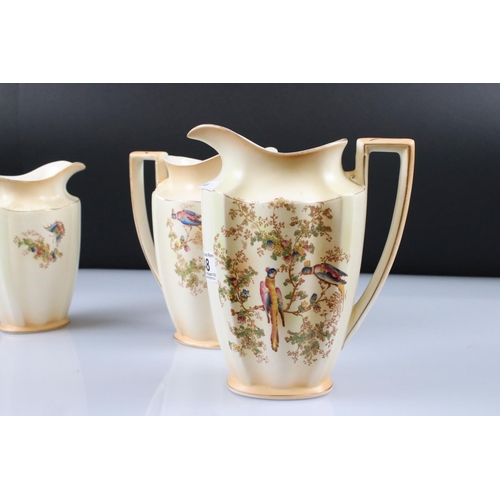 48 - Set of Three Crown Ducal Graduating Blush Ivory Jugs decorated with exotic birds, largest 22cm
