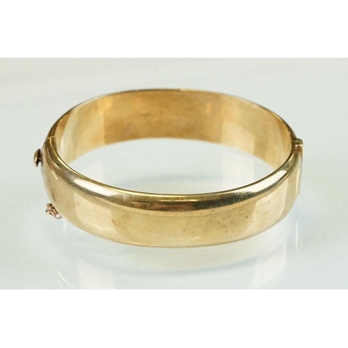 336 - 9ct yellow gold hinged bangle, the upper half with bright cut foliate scroll decoration, tongue and ... 