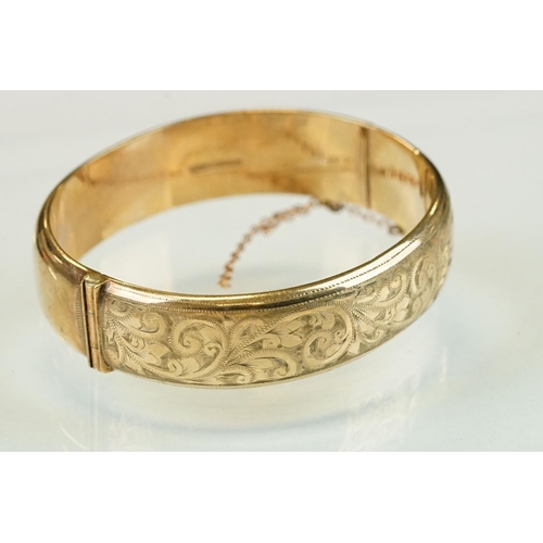 336 - 9ct yellow gold hinged bangle, the upper half with bright cut foliate scroll decoration, tongue and ... 