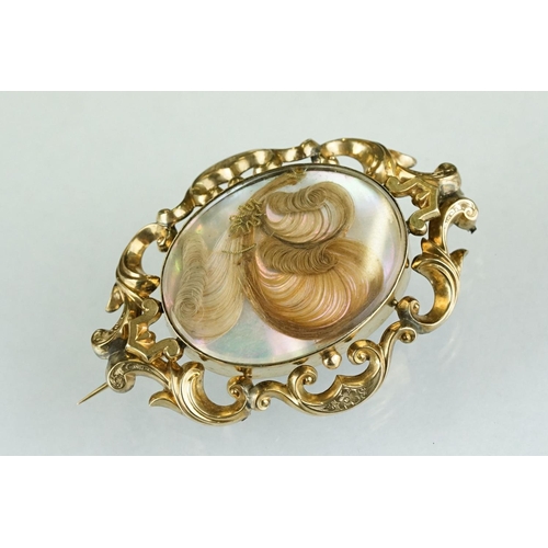 227 - A 19th century yellow metal mourning brooch with decorative scrolling, the centre piece of curled ha... 