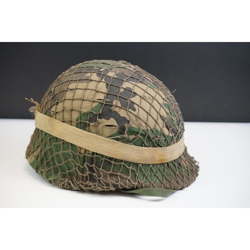 220 - A British Military Helmet Complete With Liner, Camouflage Cover, Mesh Netting And Strap.