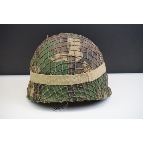 220 - A British Military Helmet Complete With Liner, Camouflage Cover, Mesh Netting And Strap.