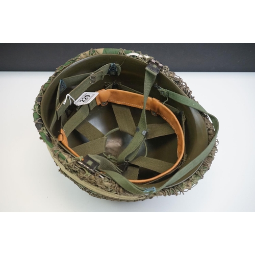 220 - A British Military Helmet Complete With Liner, Camouflage Cover, Mesh Netting And Strap.