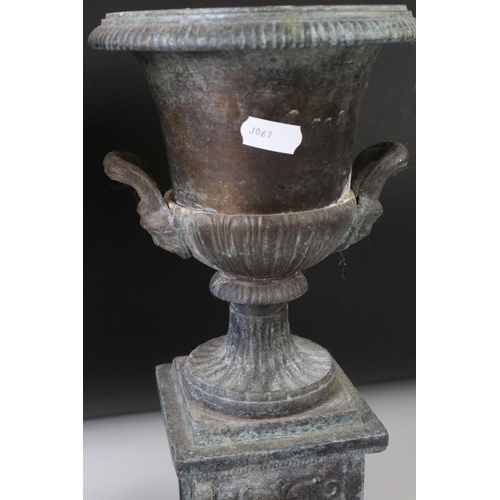 145 - Pair of bronze twin-handled urns mounted on square spelter columns with relief cast scrolling and fo... 
