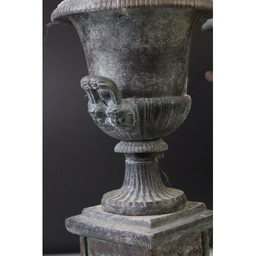 145 - Pair of bronze twin-handled urns mounted on square spelter columns with relief cast scrolling and fo... 
