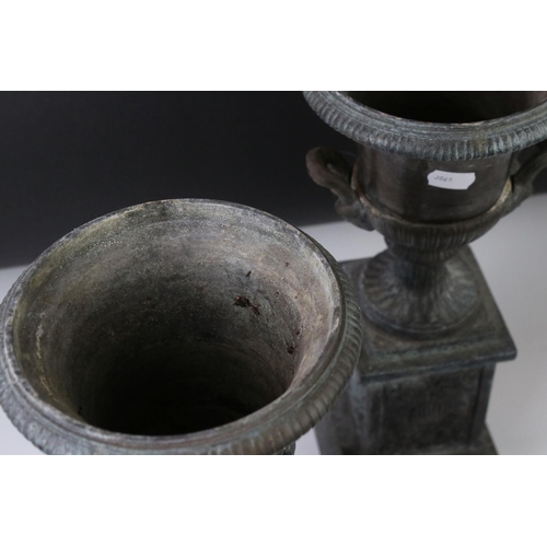 145 - Pair of bronze twin-handled urns mounted on square spelter columns with relief cast scrolling and fo... 