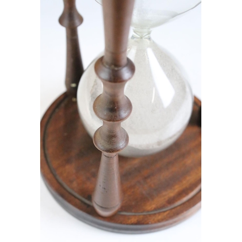 160 - Large Glass Sand Timer held on a Mahogany Circular Frame with turned supports, 24cm high