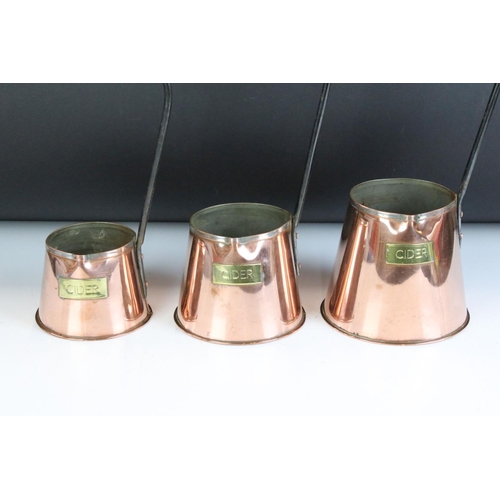 131 - Three early 20th Century copper and cast iron cider measures each of tapering form with brass labels... 