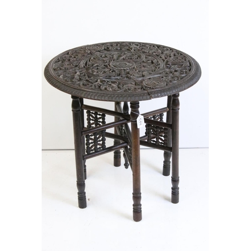 538 - Indian Hardwood Circular Table, the top profusely carved with foliate scrolling, raised in a folding... 