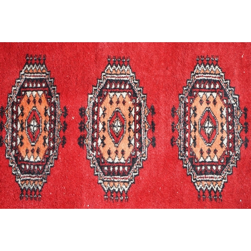 596 - Eastern Red Ground Wool Rug decorated with a row of ten guls within a border, approx. 190cm x 130cm