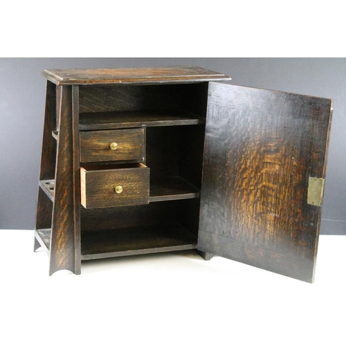 190 - Early-to-mid 20th century oak smokers cabinet of tapering form, the door opening to two drawers and ... 