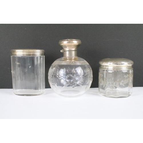 256 - A collection of antique glass jars and scent bottles with hallmarked silver tops and collars.