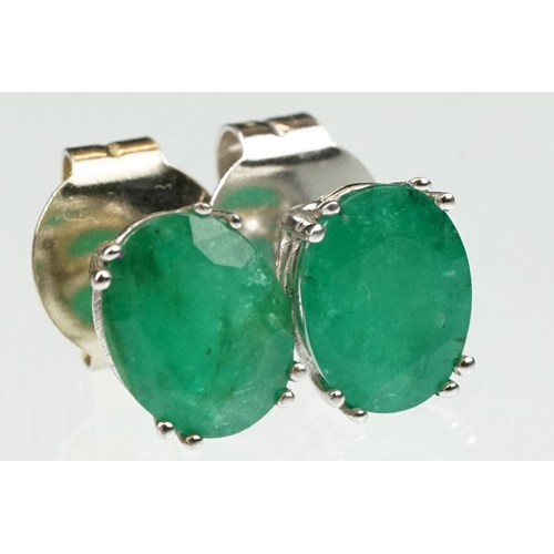 102 - Pair of emerald white metal stud earrings, the oval mixed cut emerald measuring approx 10mm x 8mm, c... 