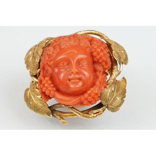 22 - 19th century coral yellow metal brooch and earrings; the brooch with carved coral putti face, surrou... 