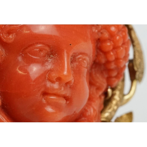 22 - 19th century coral yellow metal brooch and earrings; the brooch with carved coral putti face, surrou... 