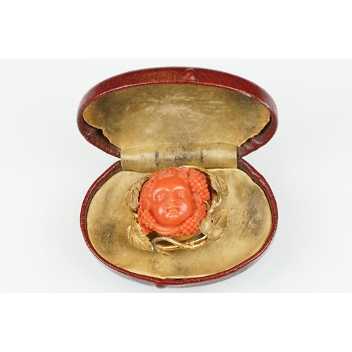 22 - 19th century coral yellow metal brooch and earrings; the brooch with carved coral putti face, surrou... 