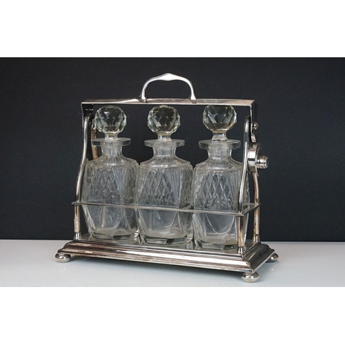 158 - Early-to-mid 20th C silver plated tantalus, housing three cut glass decanters with stoppers, raised ... 