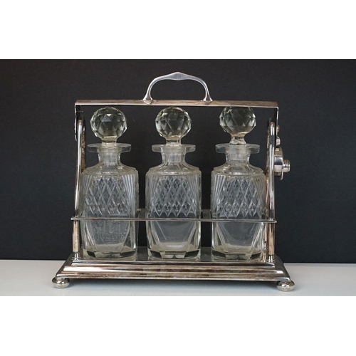 158 - Early-to-mid 20th C silver plated tantalus, housing three cut glass decanters with stoppers, raised ... 