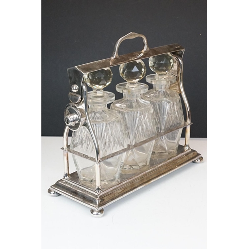 158 - Early-to-mid 20th C silver plated tantalus, housing three cut glass decanters with stoppers, raised ... 