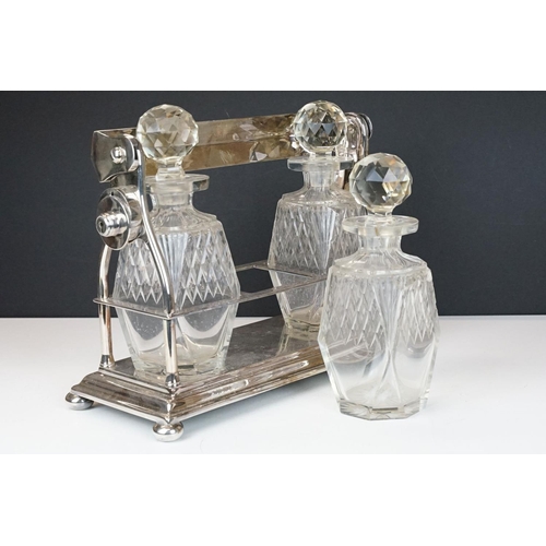 158 - Early-to-mid 20th C silver plated tantalus, housing three cut glass decanters with stoppers, raised ... 