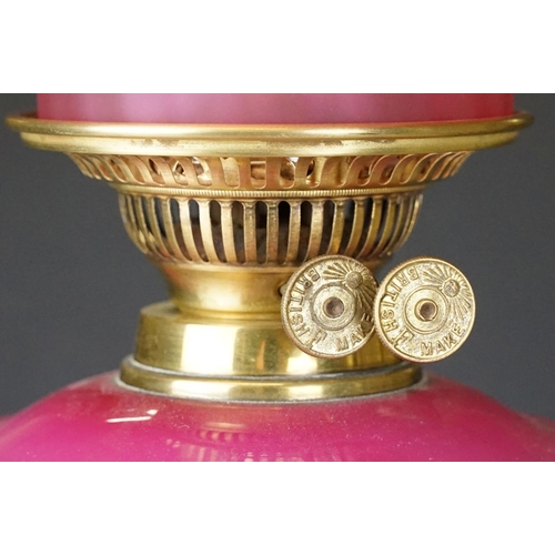 175 - Late Victorian / early 20th Century oil lamp having a round brass stepped base, pink reservoir with ... 