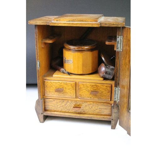 194 - Art Deco oak smokers cabinet, the glazed door opening to a tobacco pipe racks & tobacco jar above tw... 