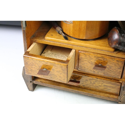 194 - Art Deco oak smokers cabinet, the glazed door opening to a tobacco pipe racks & tobacco jar above tw... 