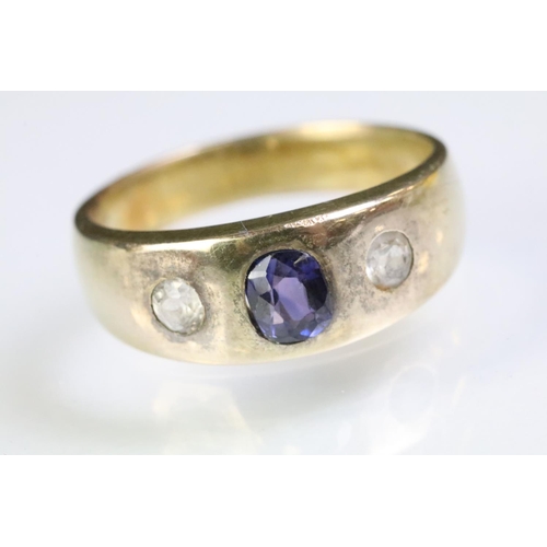 241 - Yellow metal three stone ring set with a cushion cut purple stone to the centre flanked by two round... 