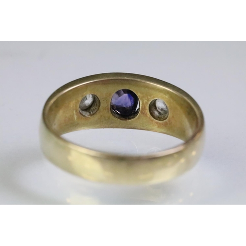 241 - Yellow metal three stone ring set with a cushion cut purple stone to the centre flanked by two round... 