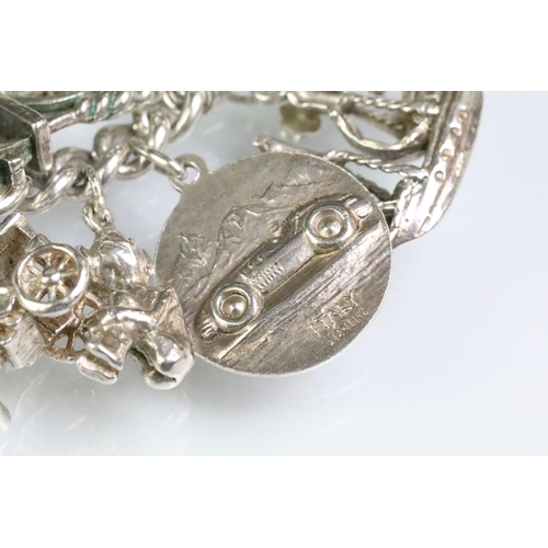 203 - Silver charm bracelet having a curb link chain with a dog lead clasp, mounted with approximately 34 ... 