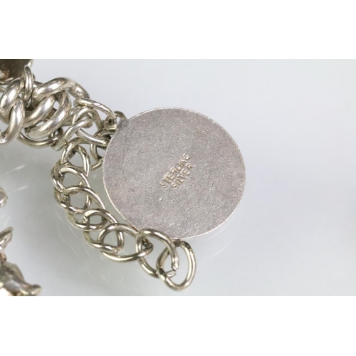 203 - Silver charm bracelet having a curb link chain with a dog lead clasp, mounted with approximately 34 ... 