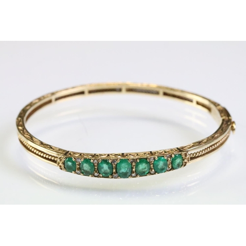 303 - Gold emerald open hinged bangle bracelet. The bracelet being set with seven oval cut emeralds with d... 