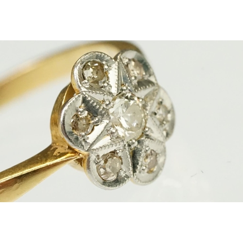 101 - 1920s 18ct gold, platinum and diamond daisy head ring being set with seven round cut diamonds on tap... 