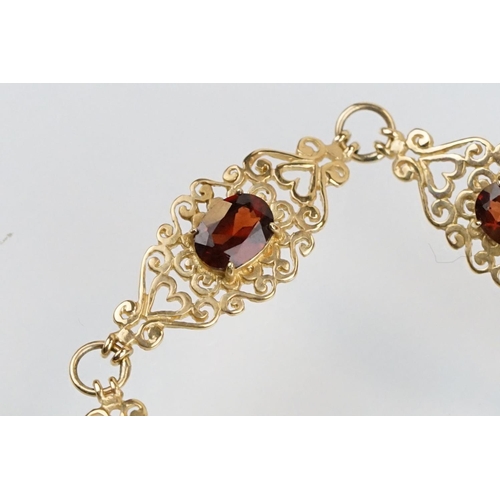 222 - 9ct gold and red stone bracelet having scrolled fret work links with an oval cut red stone to each. ... 